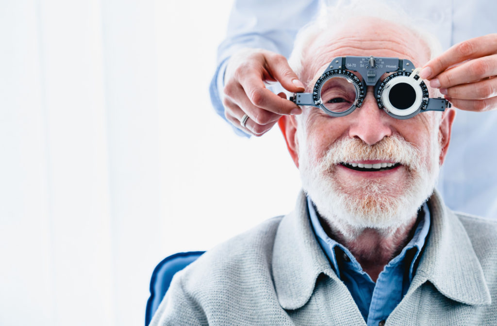 A smiling older man, sitting in a chair at the optometrist, preparing for an eye exam.