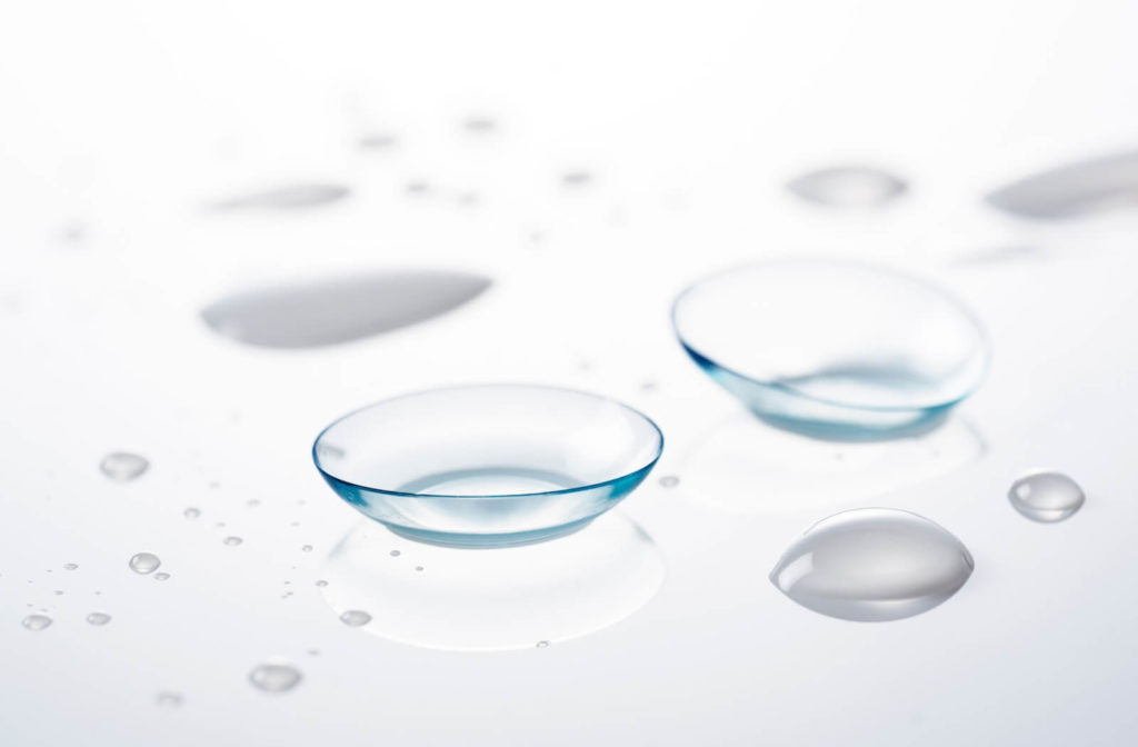 two contact lenses are on a glass surface with some saline droplets.