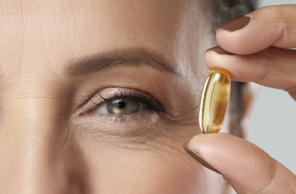 A woman holding up an Omega-3 supplement next to her eye