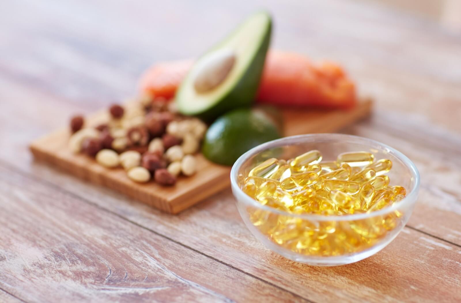 A handful of Omega-3 vitamins placed in a bowl next to various eye-healthy foods, including fish, avocados, and nuts