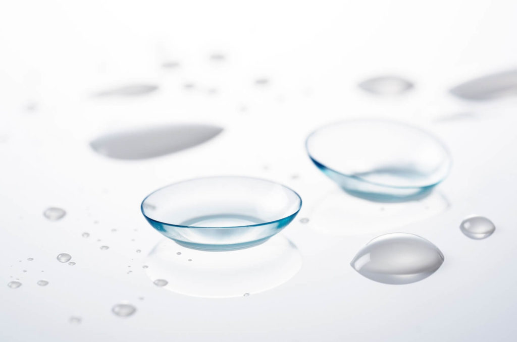 a pair of contact lenses are on a glass surface on a white background with saline droplets.