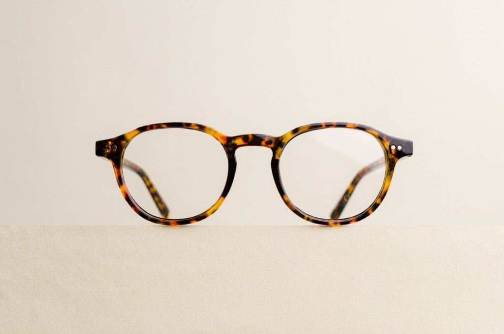 a pair of tortoise shell print glasses are on a beige background.