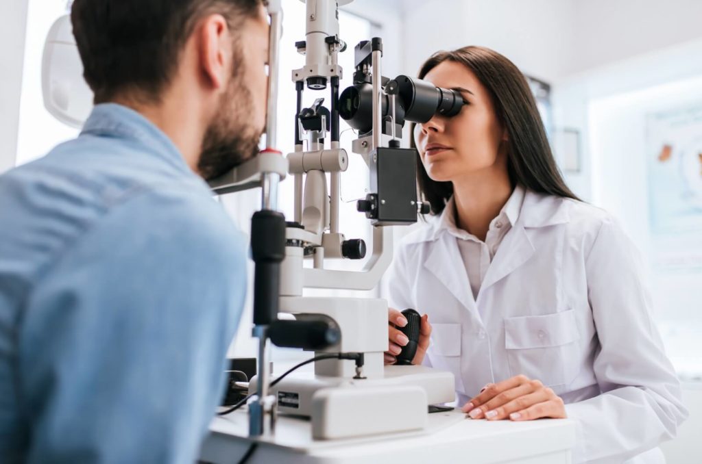 A female optometrist examining a male patient's eyes to determine if he's eligible for LASIK.