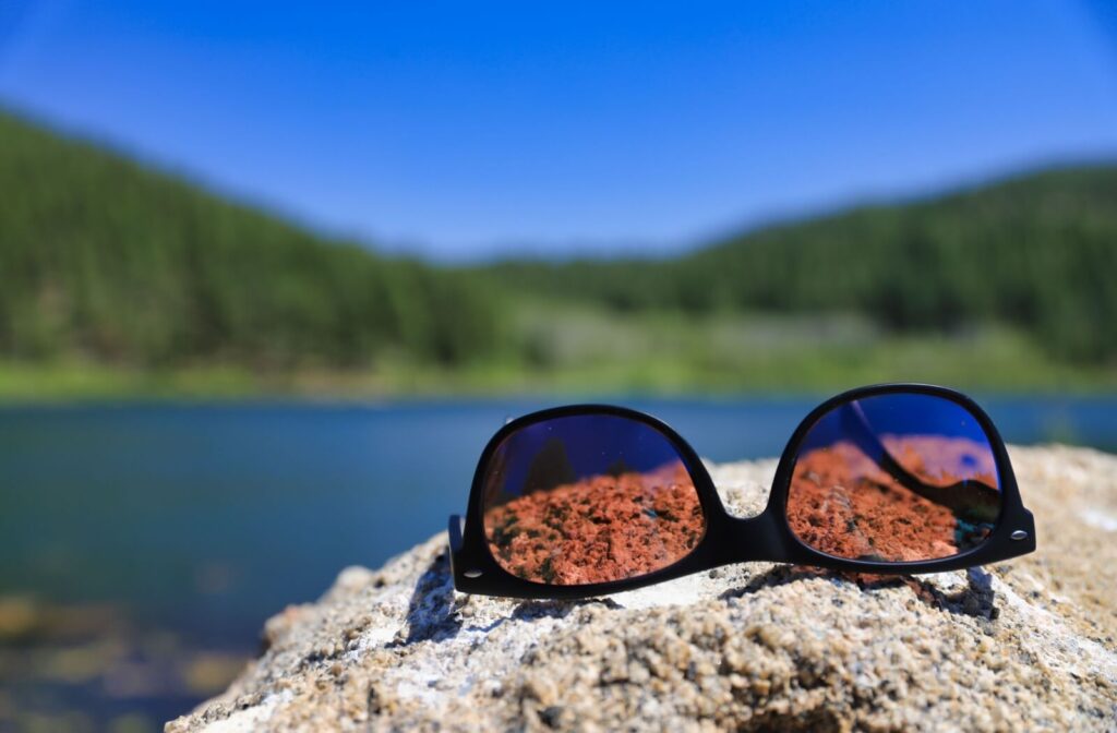 A pair of polarized sunglasses sits on top of a rock by a lake.