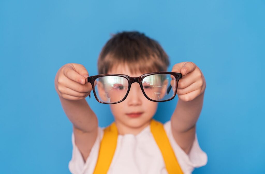 A child holding a pair of eyeglasses at arm's length.