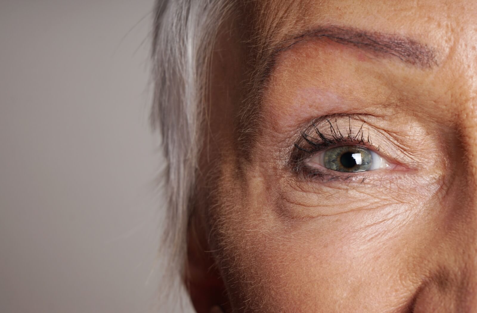 Close-up of an older adult's eye on a plain gray background.