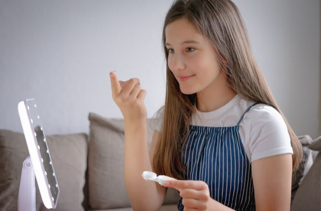 An individual holding a contact lens on their fingertip while looking into a lighted mirror.