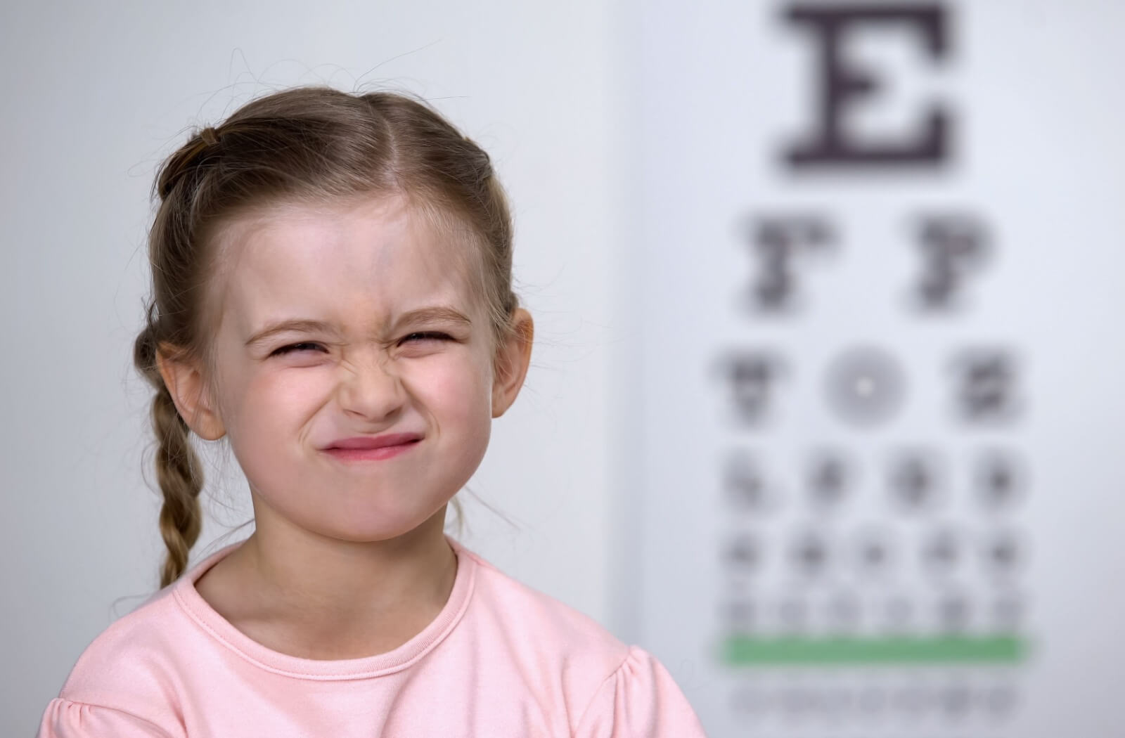 A child squinting their eyes in front of a blurred vision chart during an eye exam.