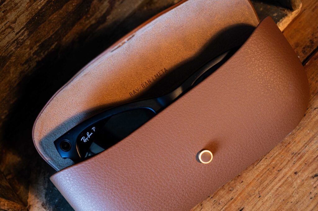 A top-down view of black Ray-Ban Meta smart glasses resting inside an open brown leather protective charging case on a rustic wooden surface.